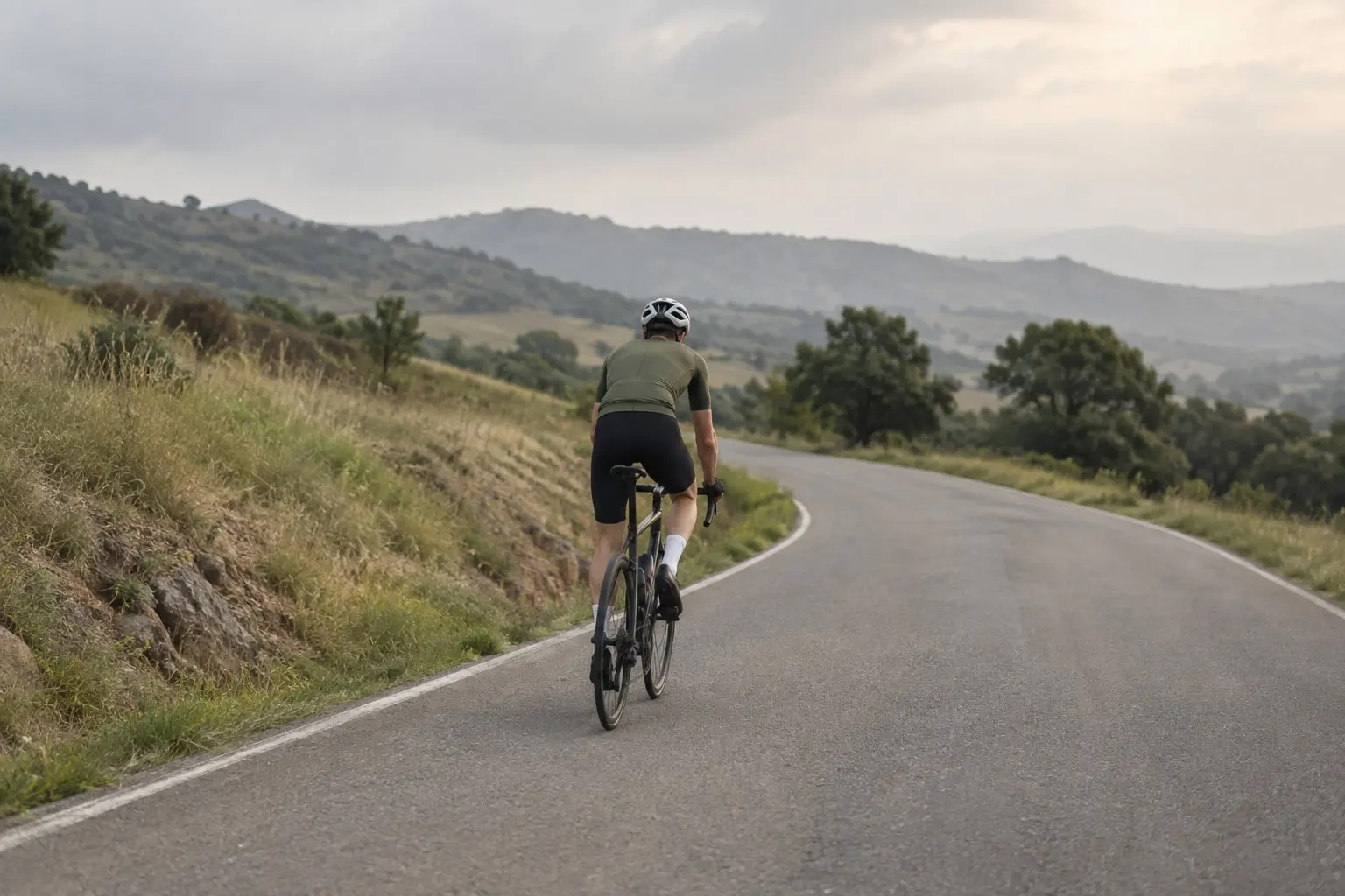 A road cyclist riding away along a quiet road through grassy hills